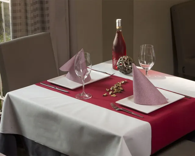 Mesa con mantel blanco, camino burdeos y servilletas rosas plegadas