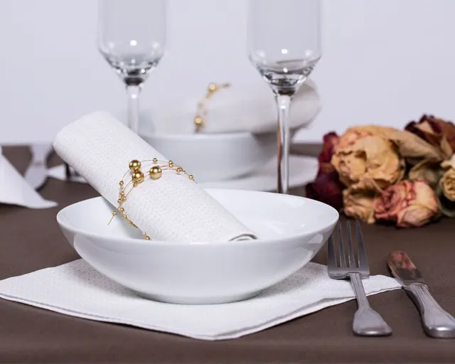 Mantel marrón con servilleta blanca enrollada y servilletero dorado