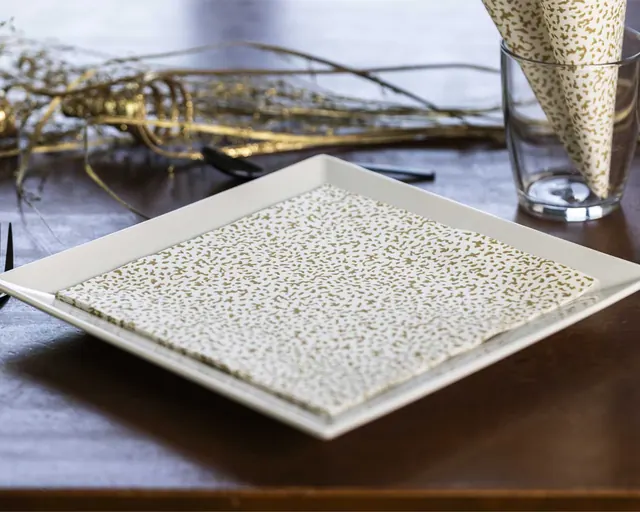 Servilleta con estampado dorado sobre plato cuadrado blanco