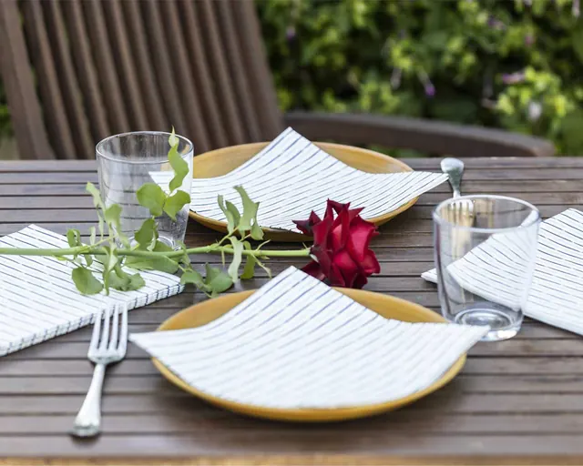 Servilletas de rayas en mesa de terraza con una rosa roja